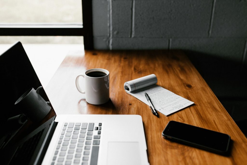 MacBook Pro, taza de cerámica blanca y teléfono inteligente negro sobre la mesa